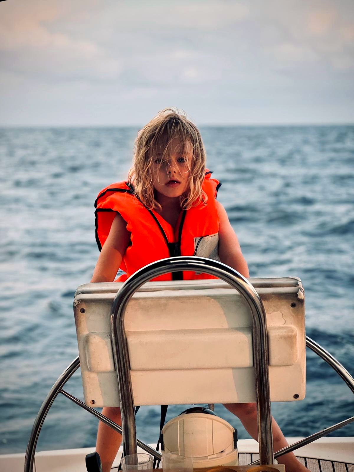 Child wearing a life jacket at the helm of a sailing boat
